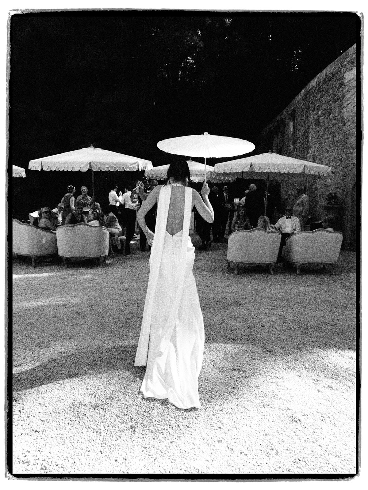 The bride under a parasol among the guests, in black and white