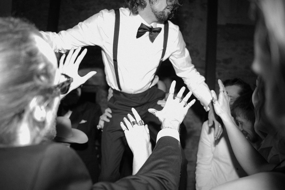 The groom being helped with his bow tie, in black and white