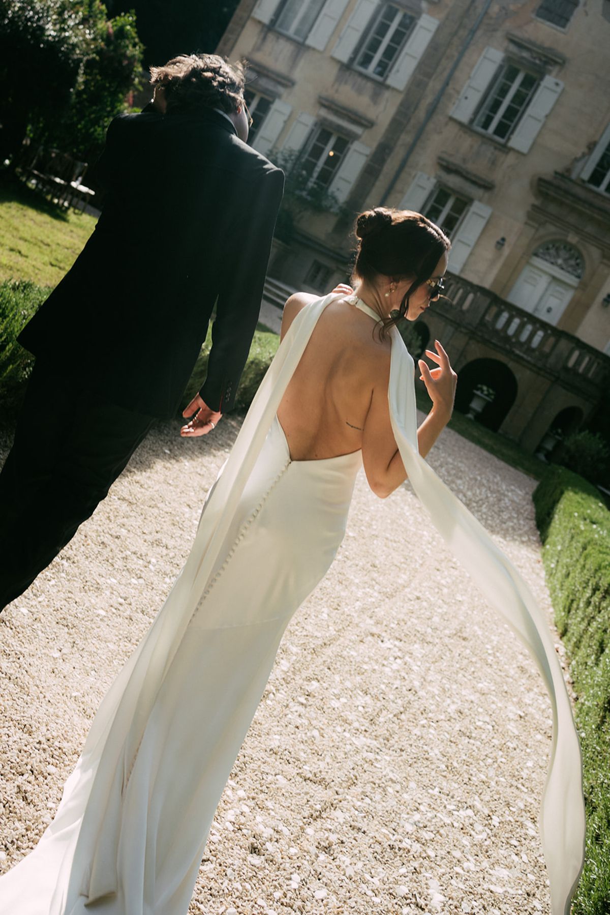 The bride walking away along the gravel, her veil trailing
