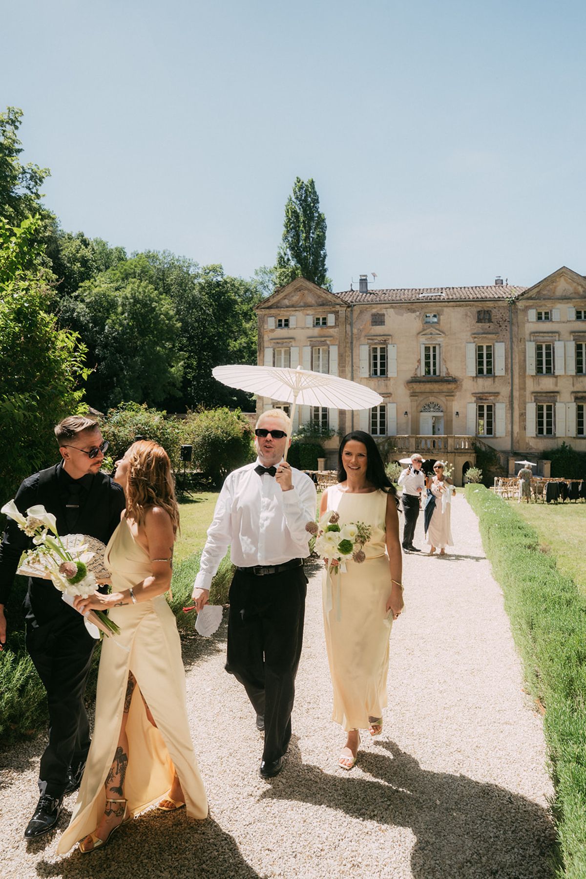 Guests walking up to the chateau with parasols and bouquets