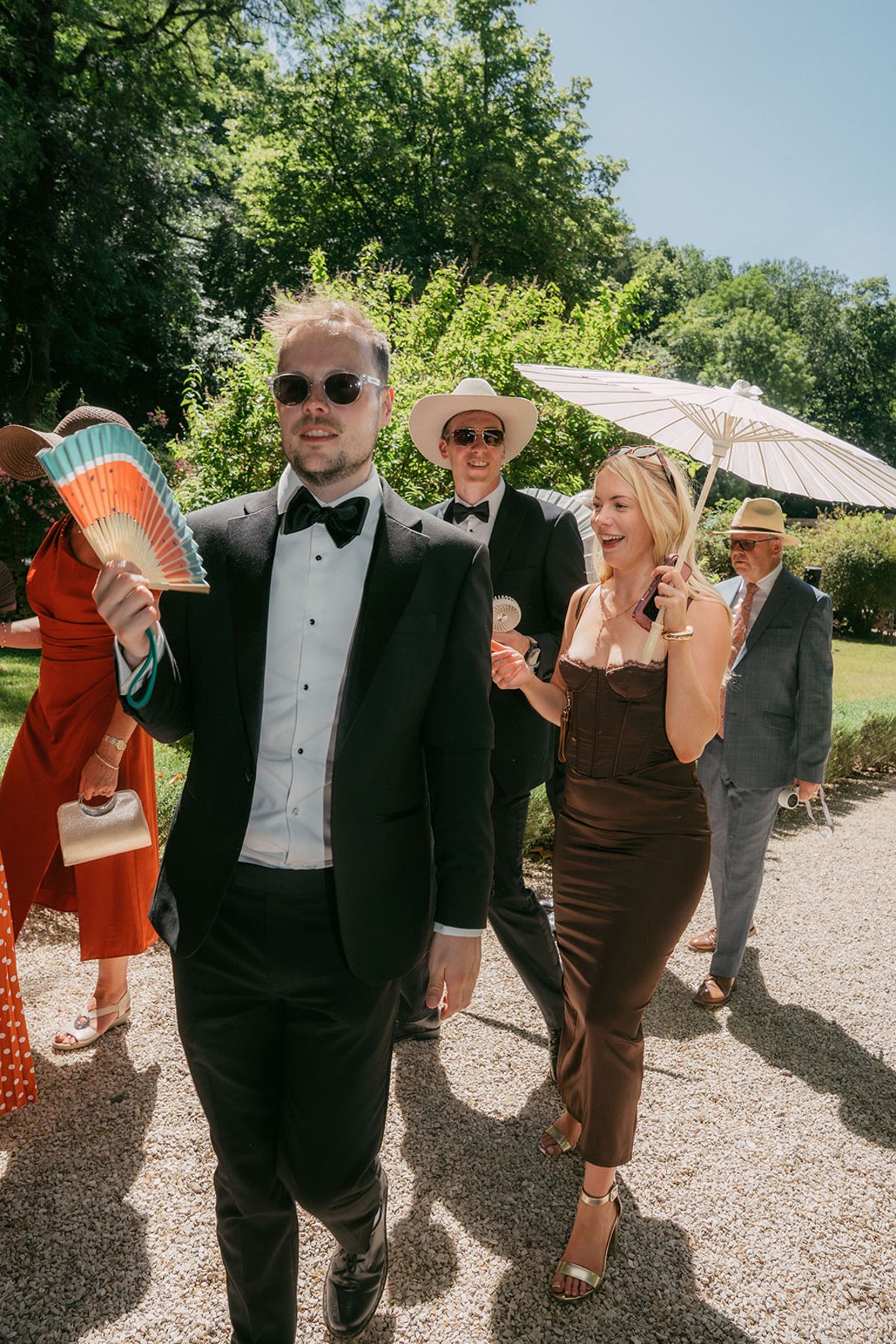 Guests walking with fans and parasols in the afternoon sun