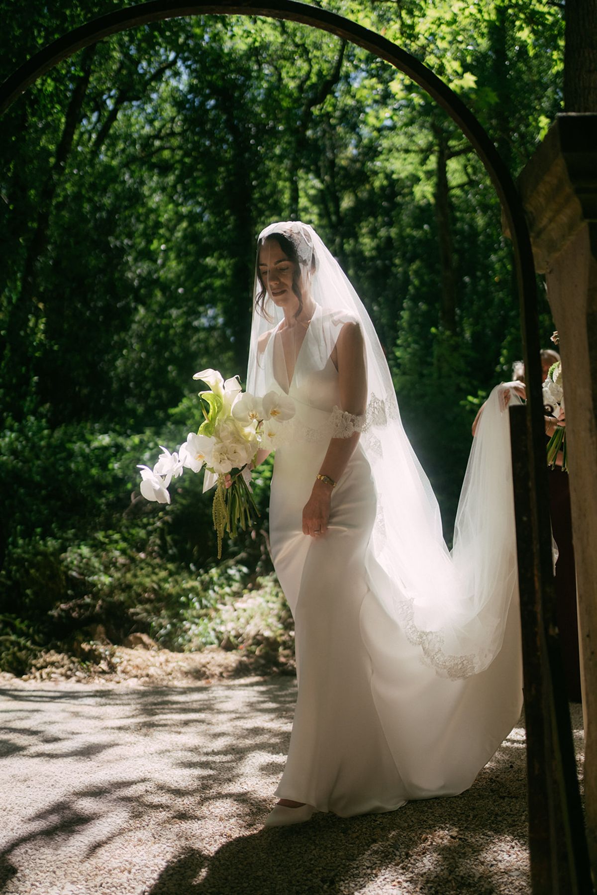The bride carrying her bouquet beneath a garden arch
