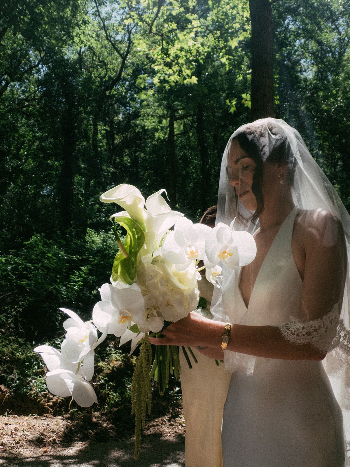 The bride holding a white orchid and calla bouquet in the woods