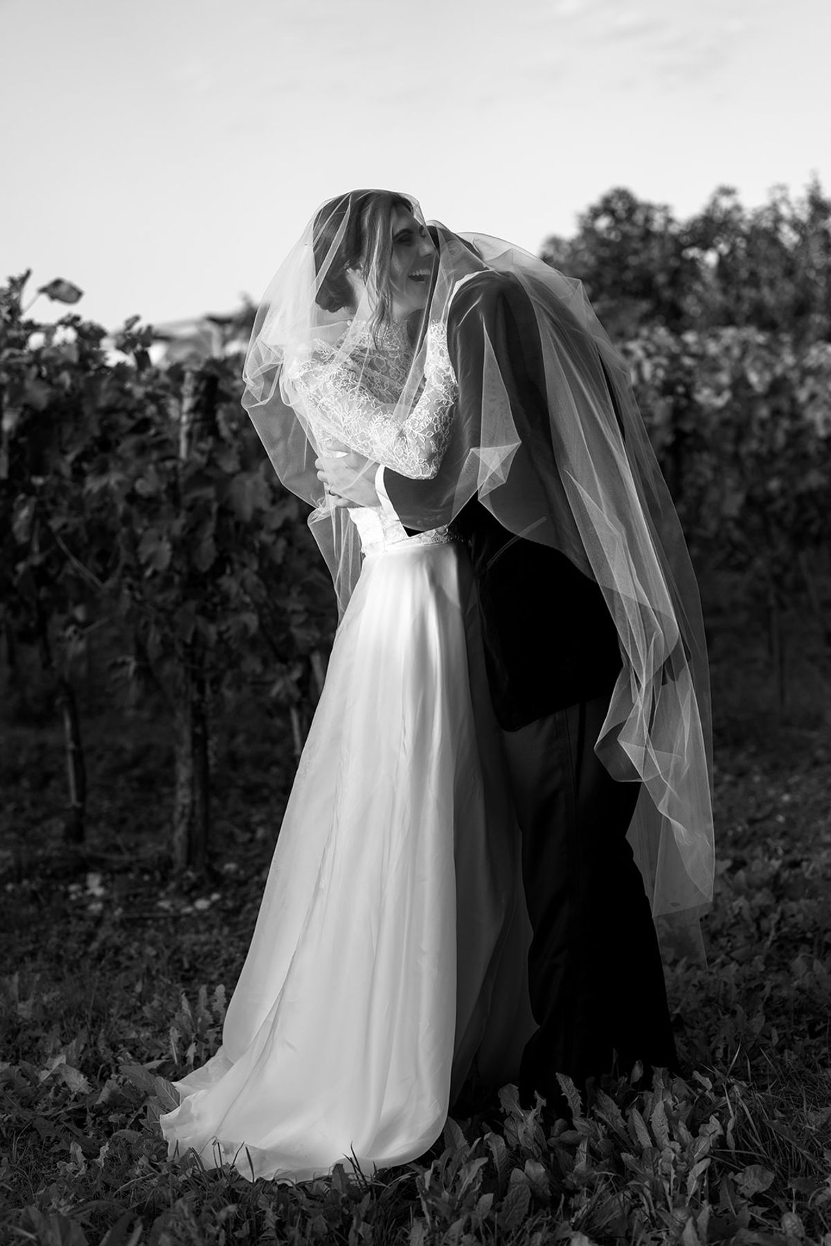 The couple kiss beneath the bride's veil among vines, in black and white.