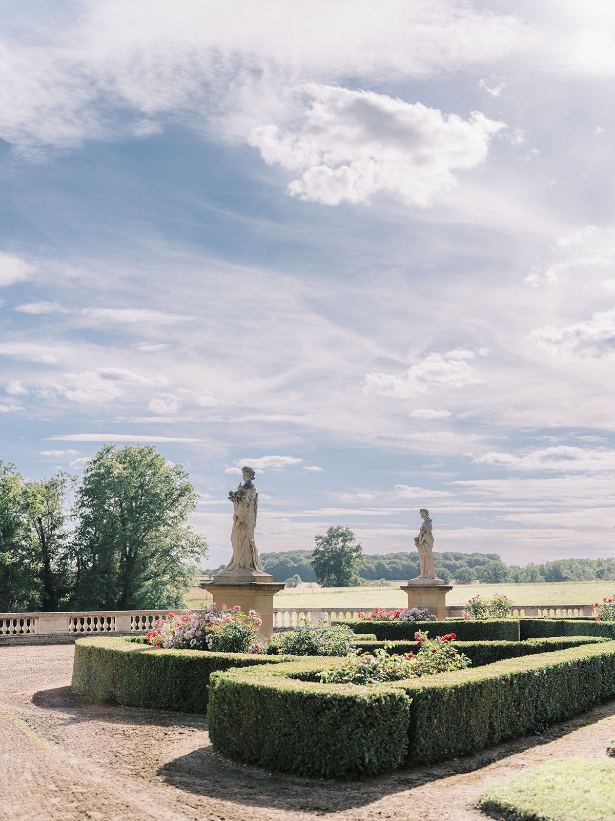 The formal parterre and statuary at La Chassagne under a summer sky