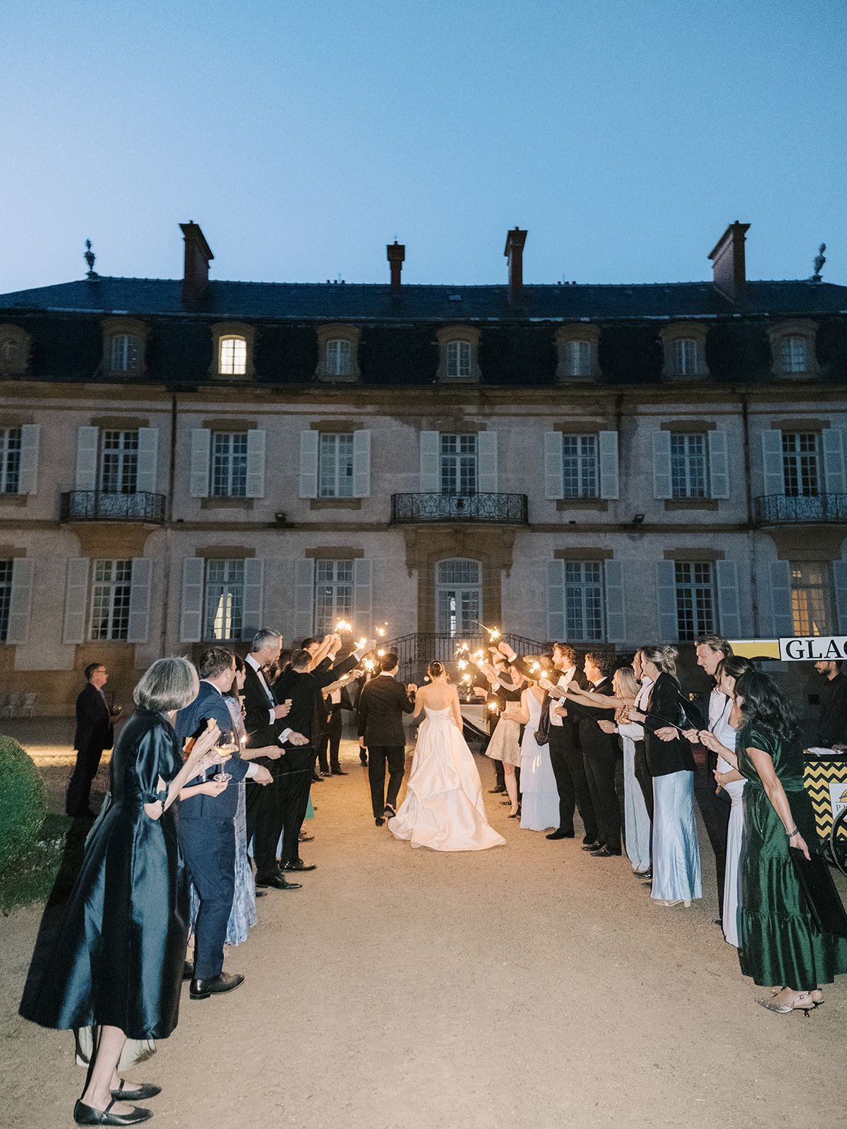 Guests holding sparklers as Haley and Tyler pass, the chateau lit behind