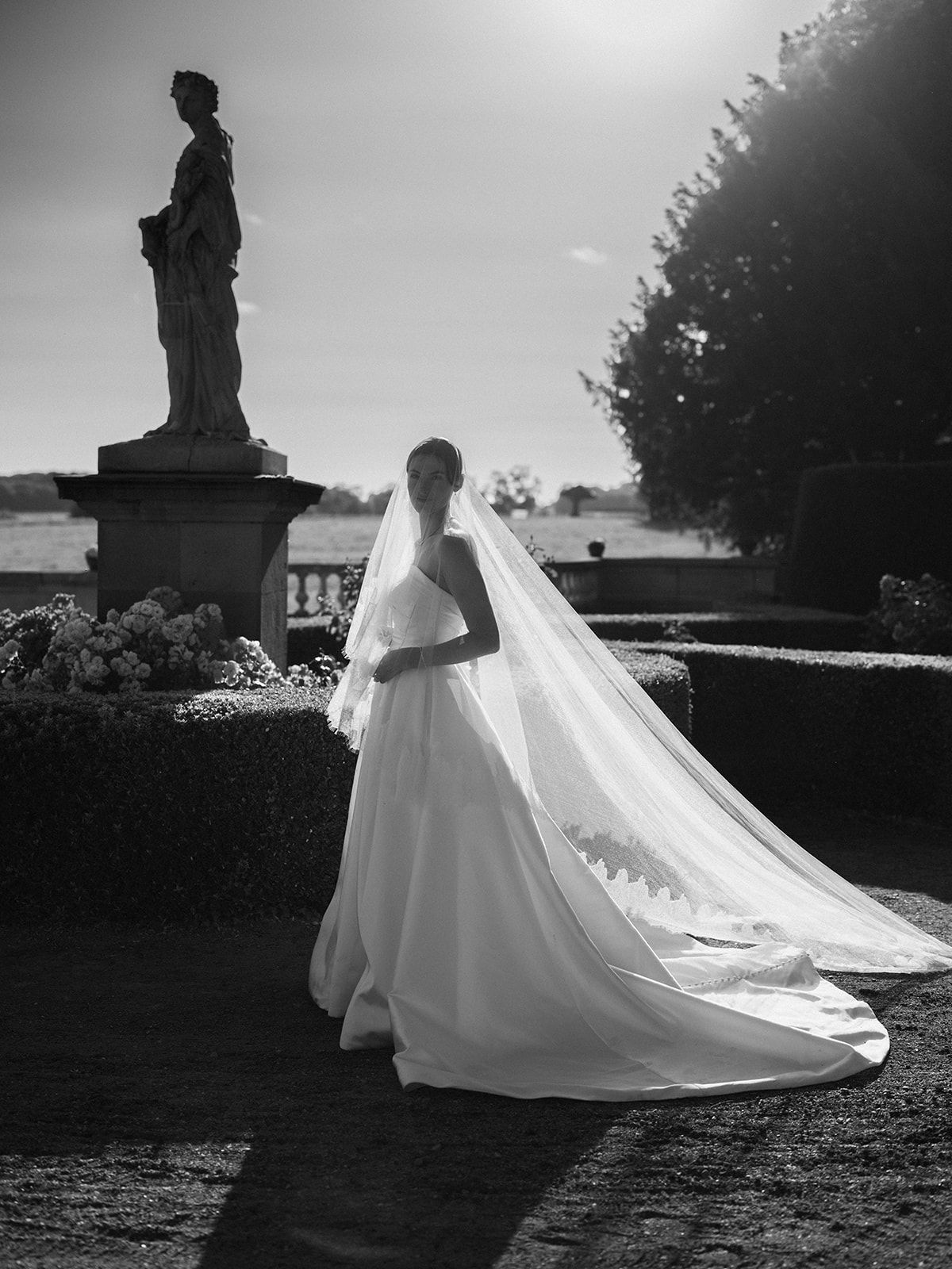 Haley in her gown and cathedral veil beside the statue