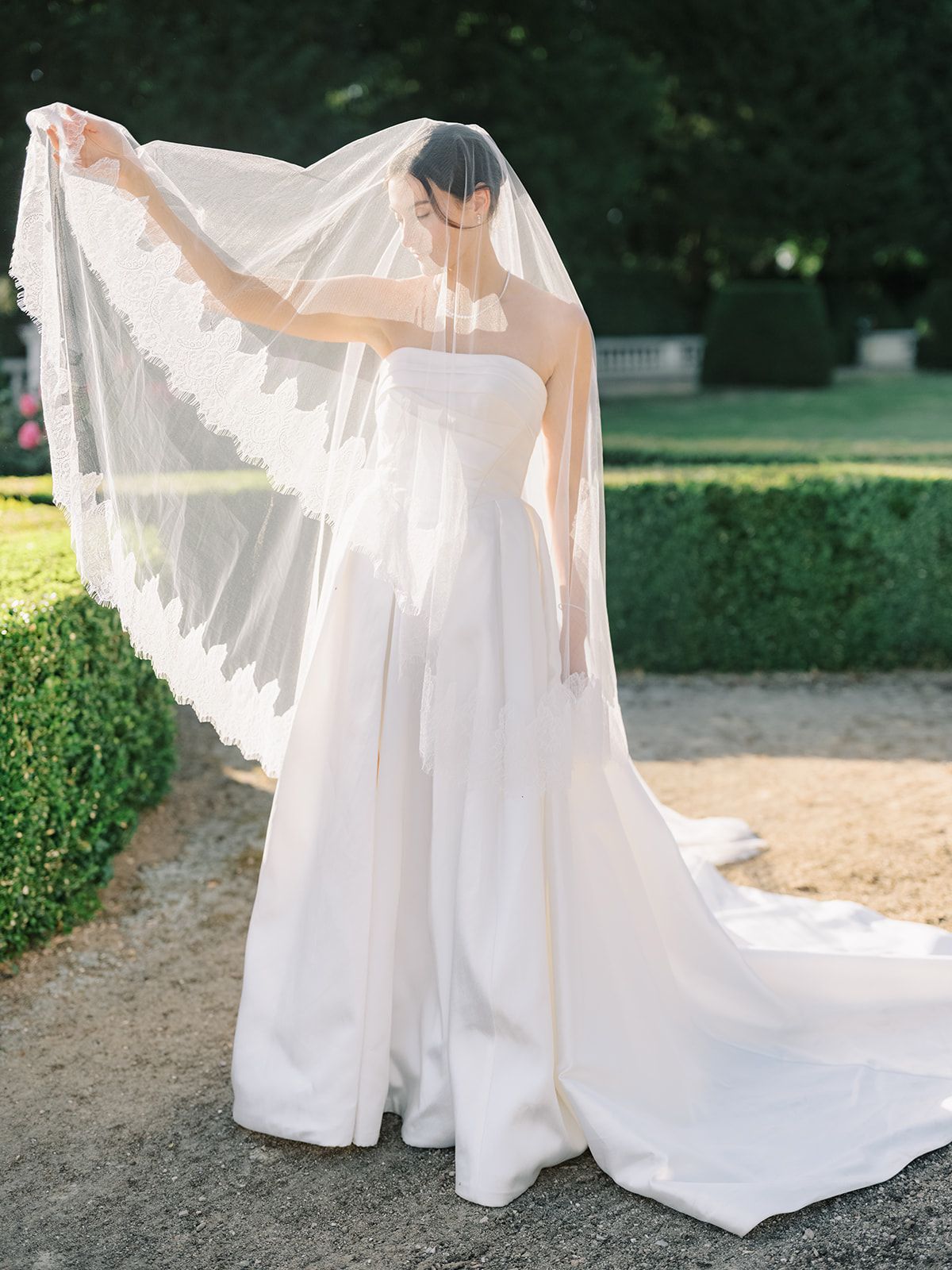 Haley holding her cathedral veil open along the garden path