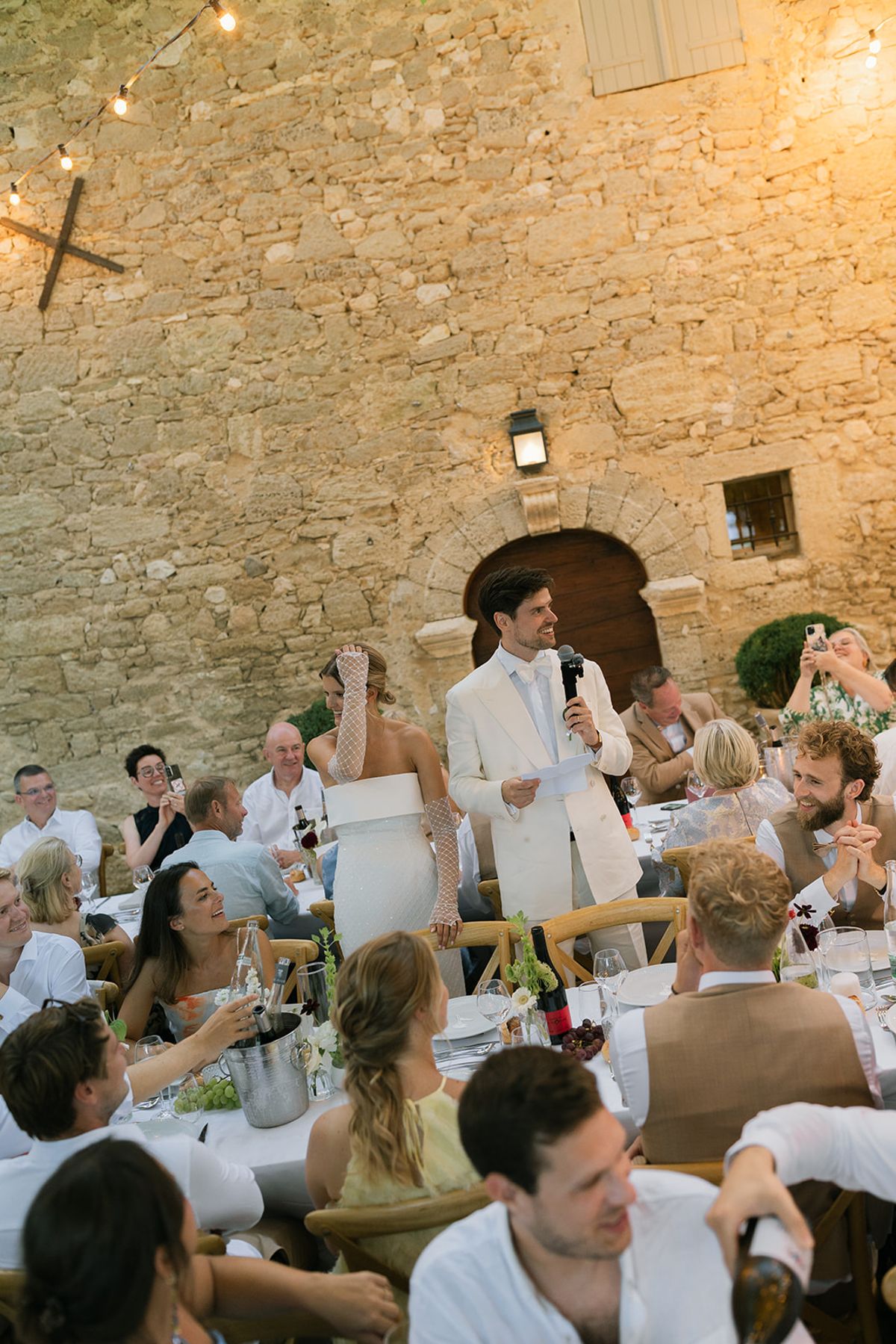 The groom gives a speech with a microphone beside the bride during dinner