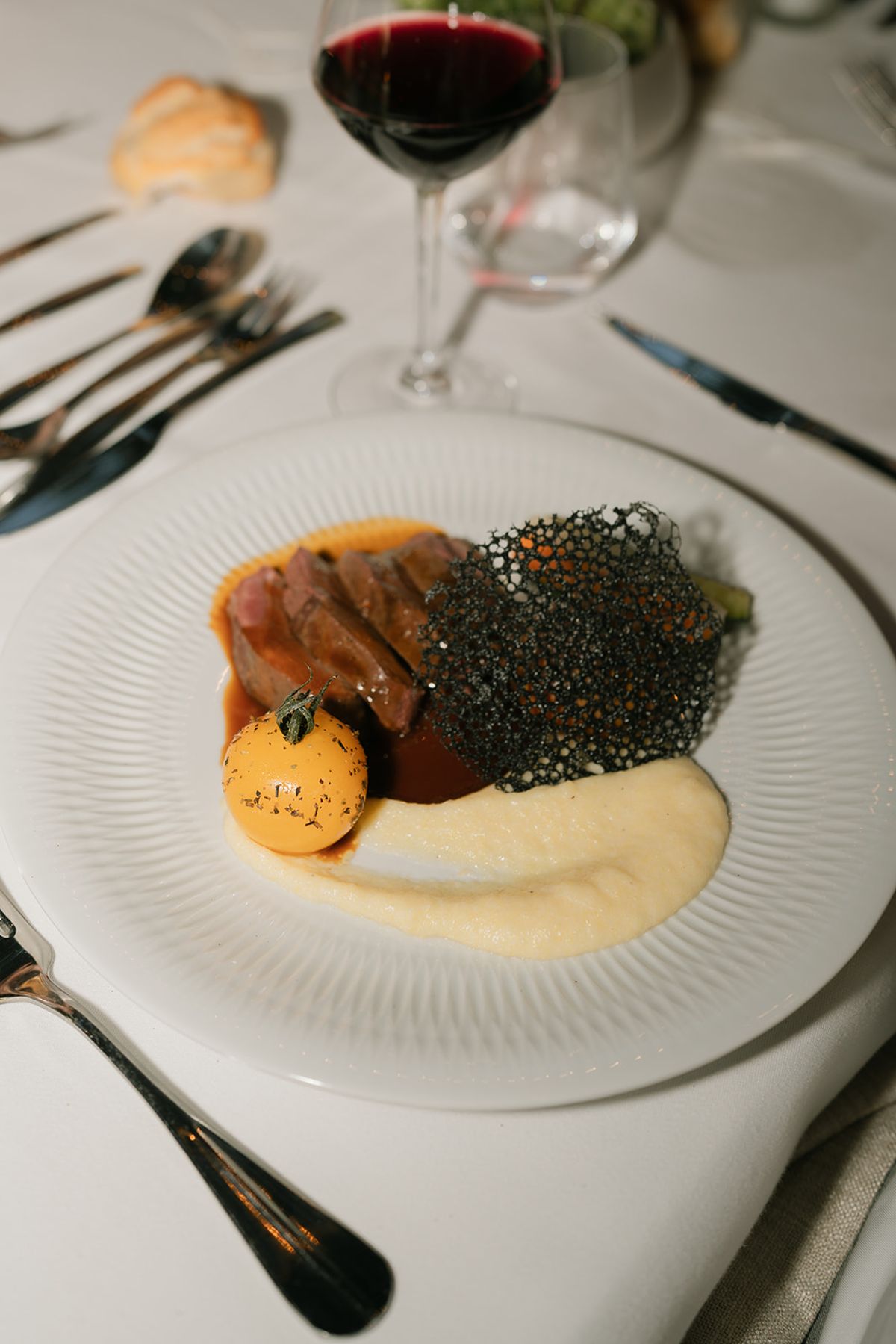 A plated main course with a crisp tuile and a glass of red wine