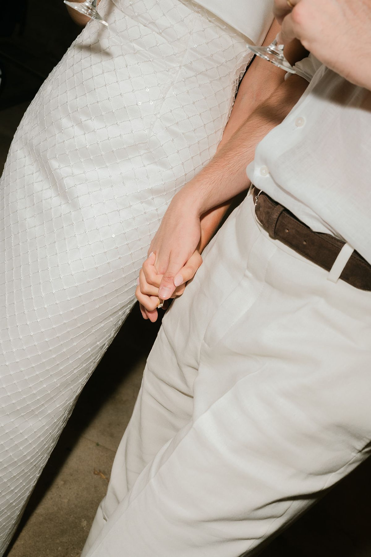 The bride and groom holding hands, a close view of her grid-pattern dress and his white trousers