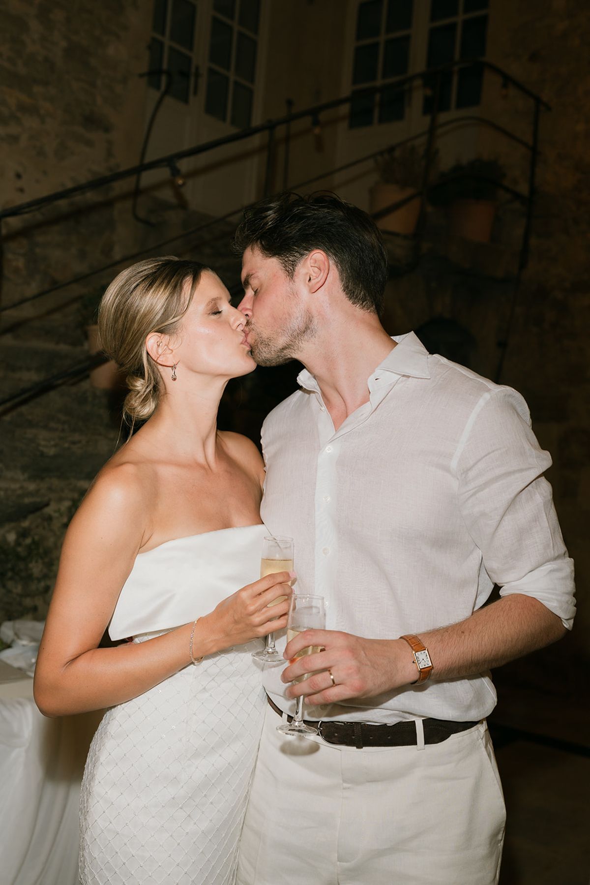 Jolien and Maxime kiss with glasses in hand after dark in the courtyard
