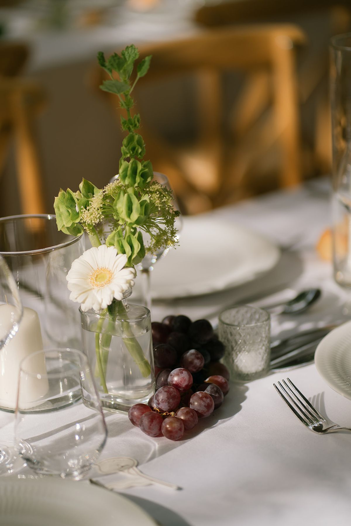 A table centrepiece of small white flowers and red grapes on white linen