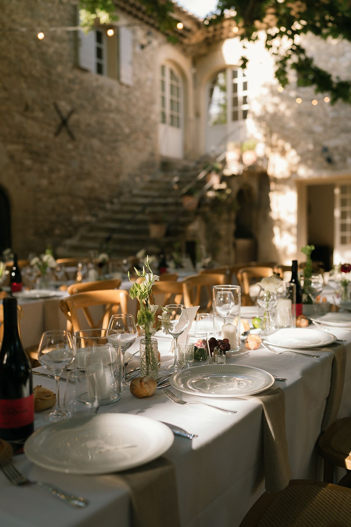 Place settings and wine glasses on a long table in the courtyard