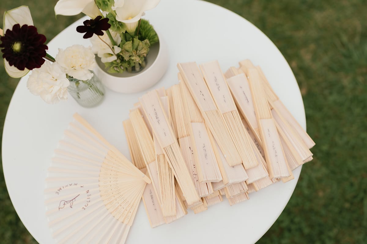 Personalised wooden fans for guests on a round table beside white and dark red flowers