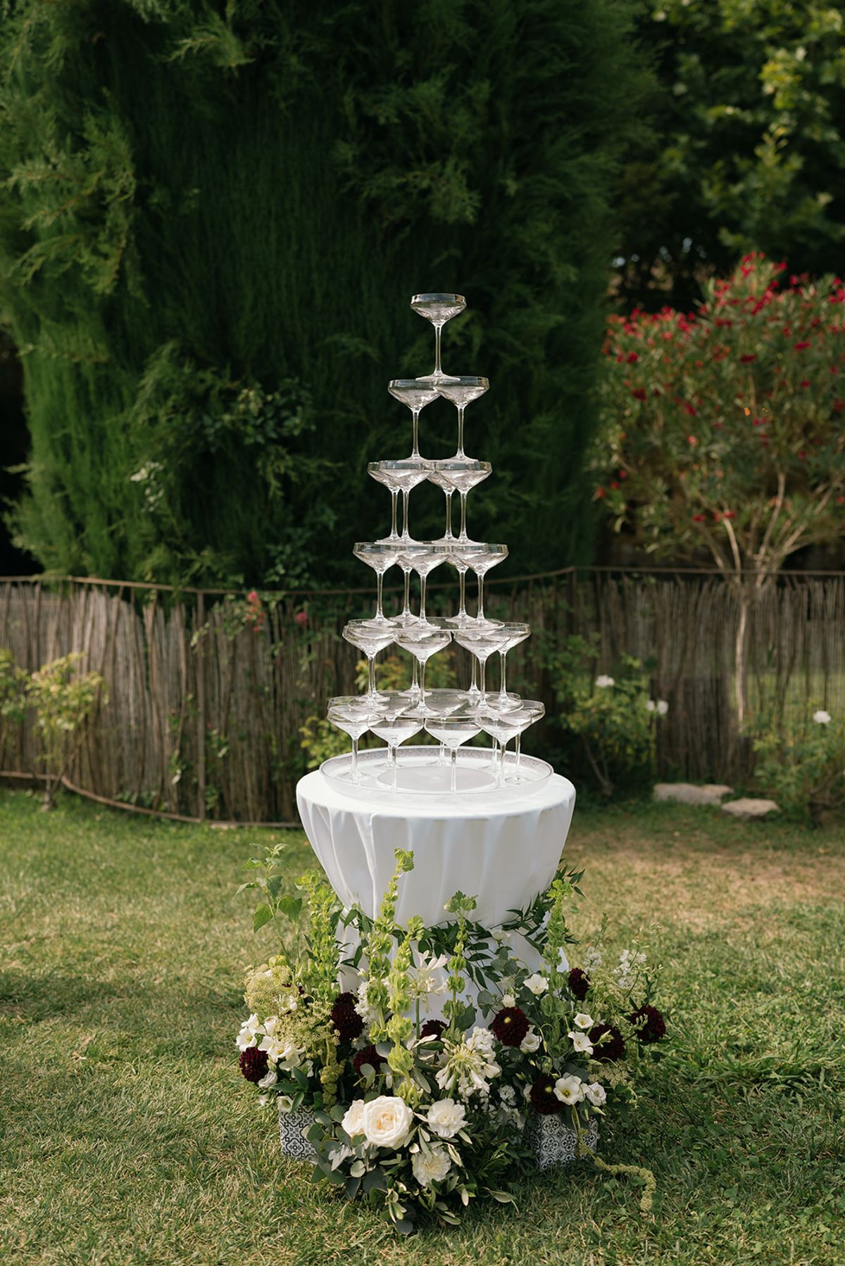 The champagne coupe tower on the lawn with white and dark red flowers at its base