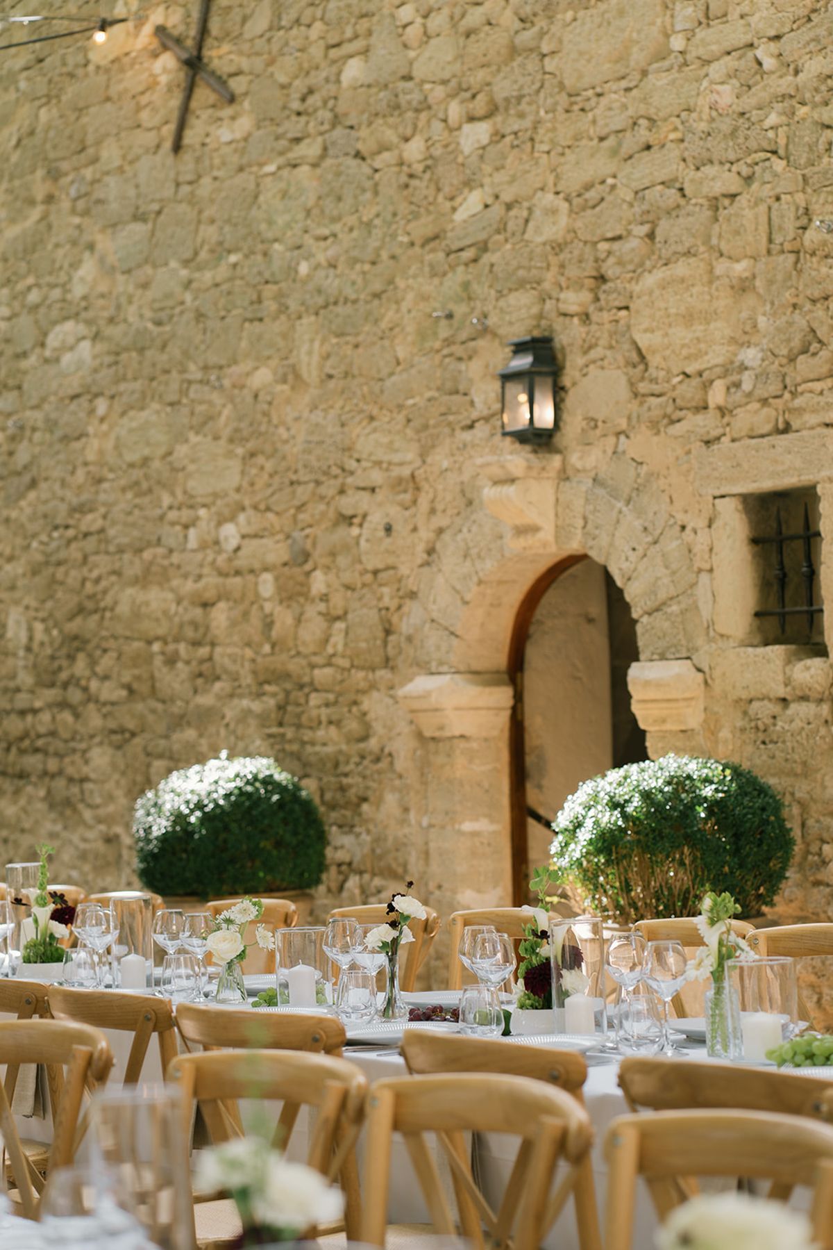 Dinner tables set in front of a stone doorway with clipped box balls in the courtyard