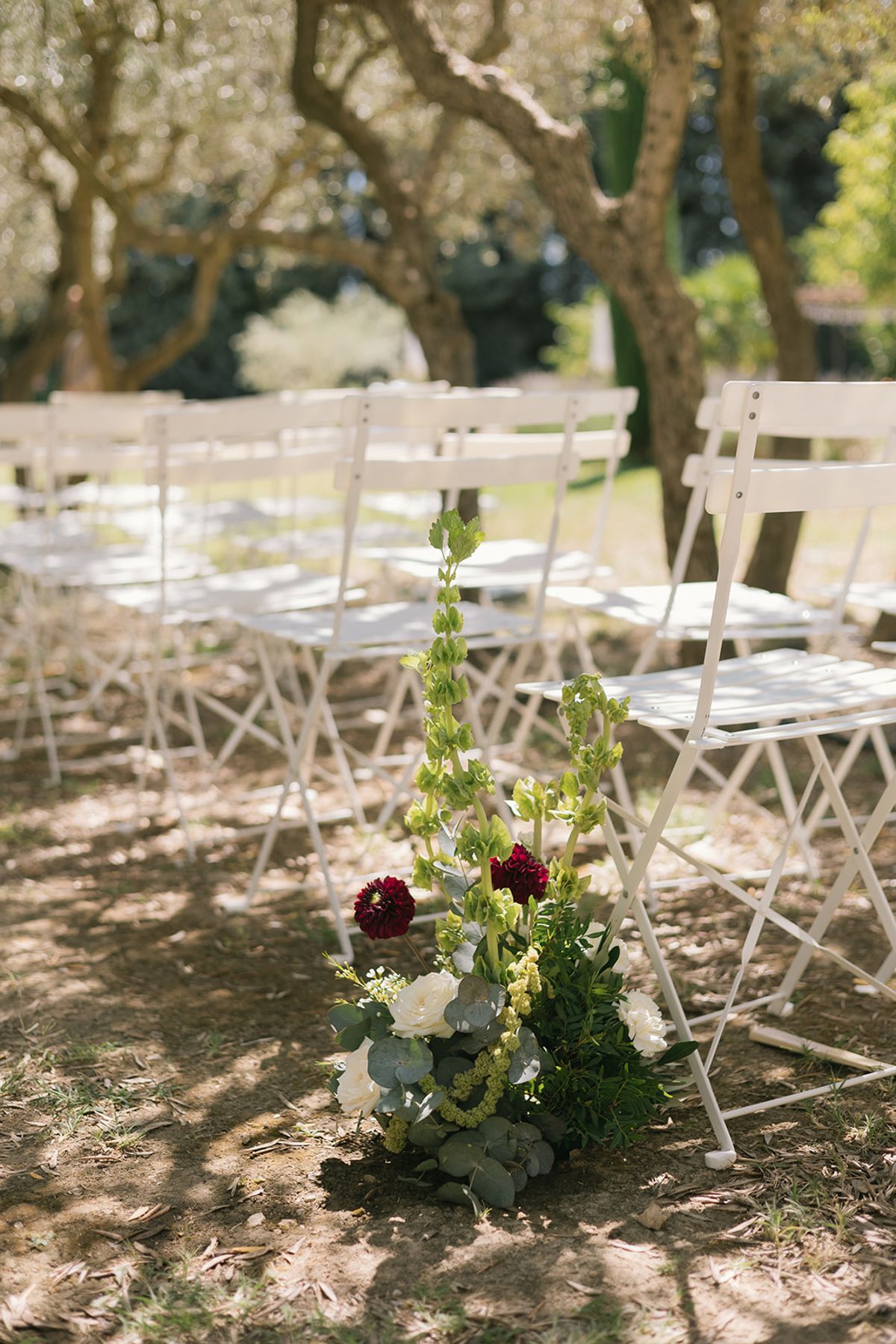 White folding chairs and a floral arrangement at the end of a ceremony row in the olive grove