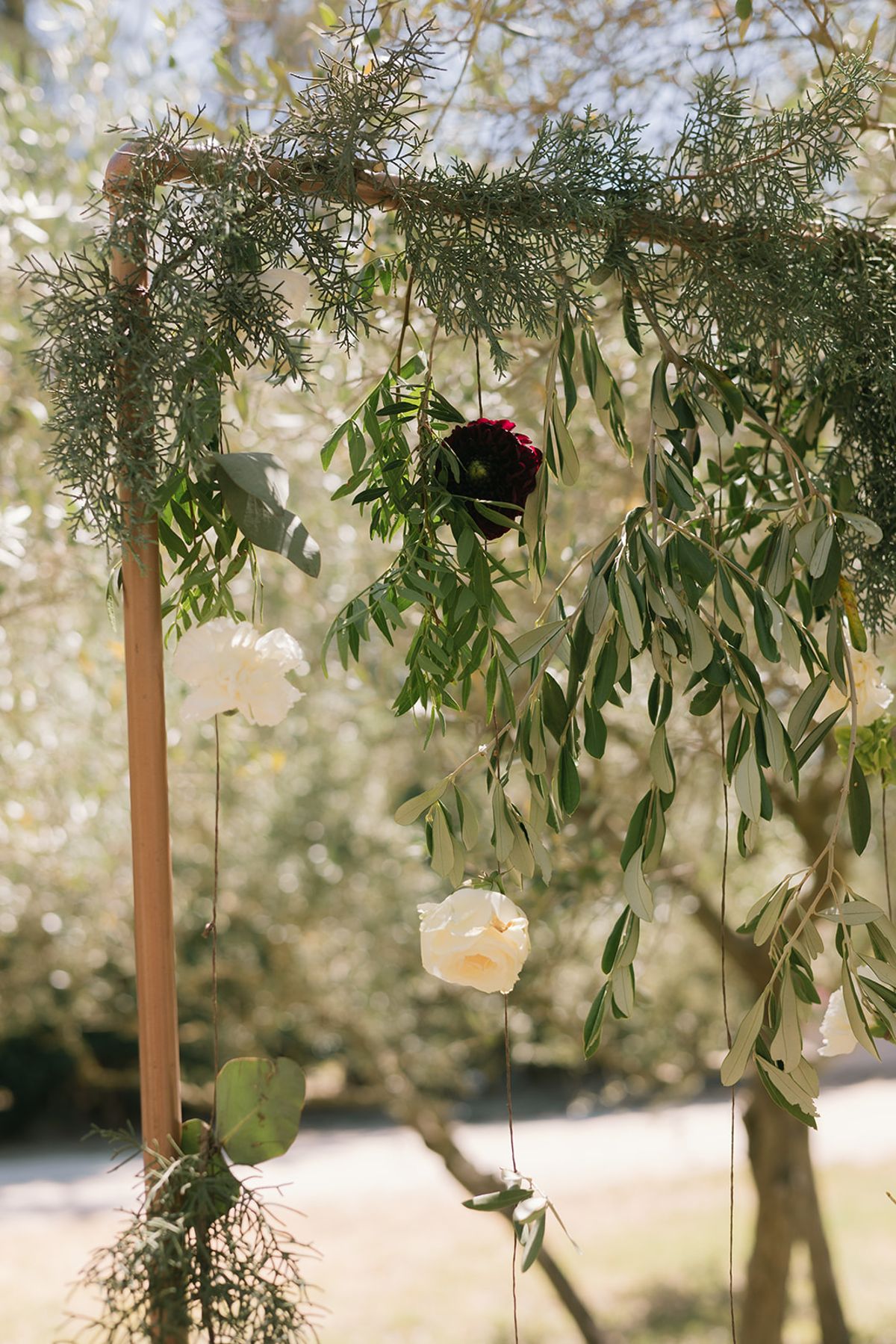 The ceremony arch hung with greenery, white flowers and a dark red bloom