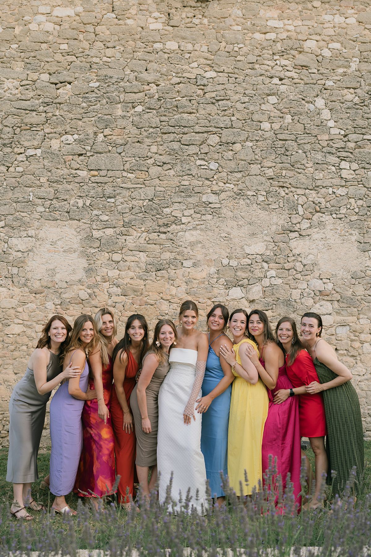 The bride with her friends in brightly coloured dresses in front of a stone wall