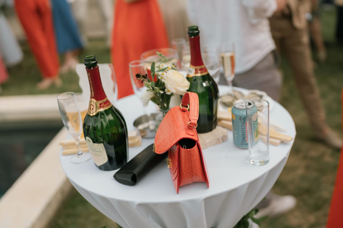Champagne bottles and a guest's red handbag on a poolside table