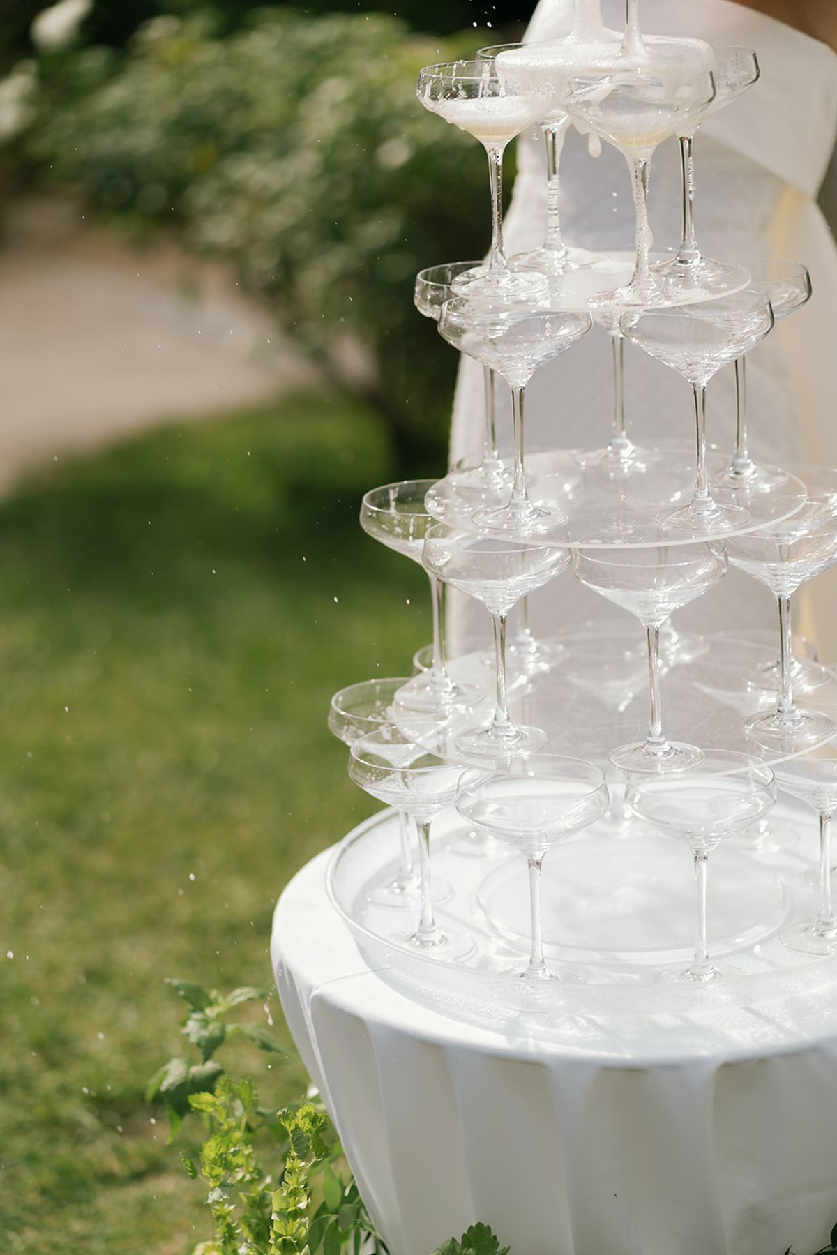 A tower of champagne coupes on a white-clothed table on the lawn