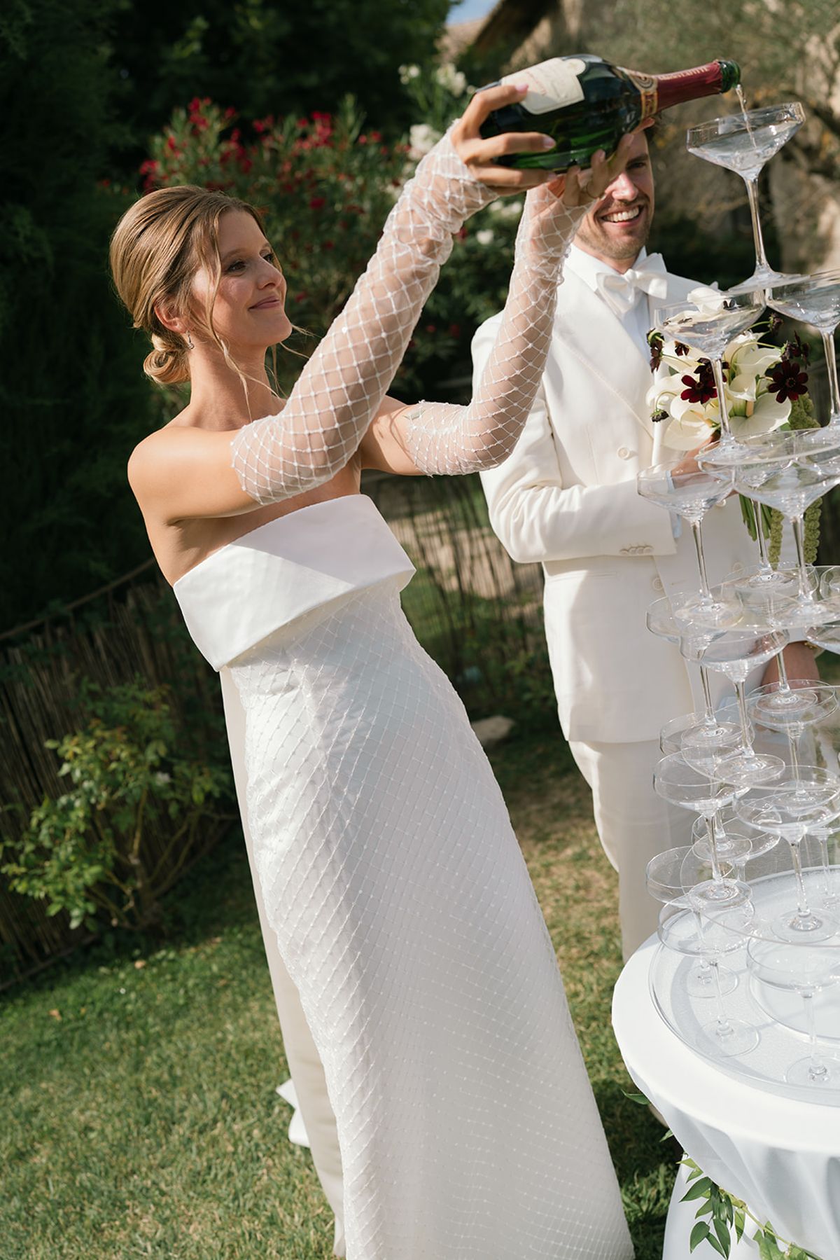 The bride pours champagne over the coupe tower beside the groom