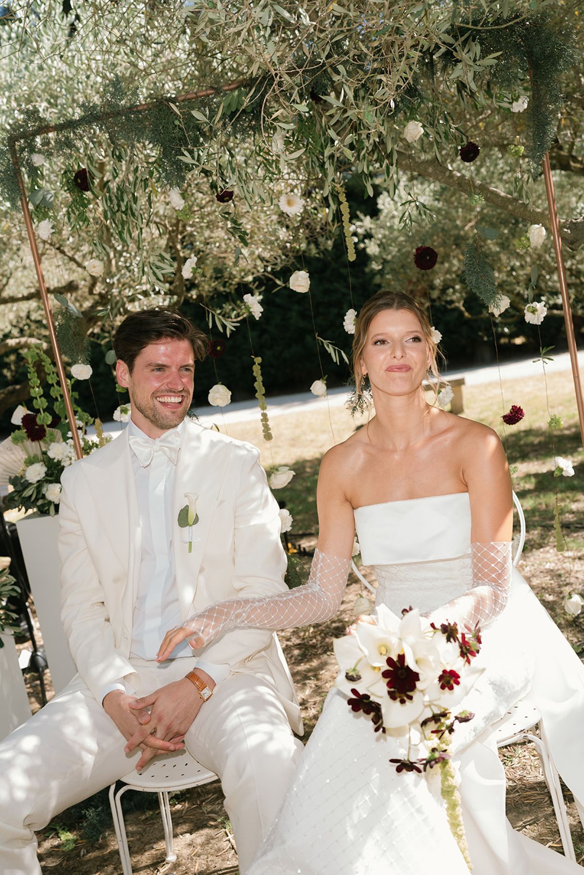 The bride and groom laughing in their ceremony chairs beneath the olive trees
