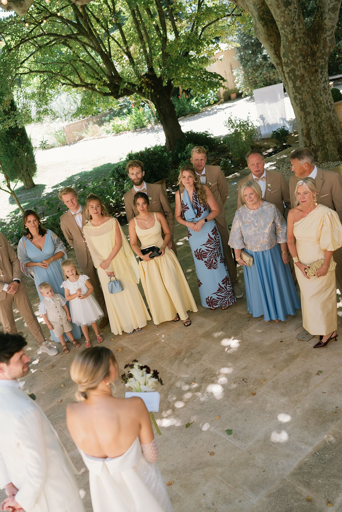 The bride and groom facing family and friends gathered beneath the trees