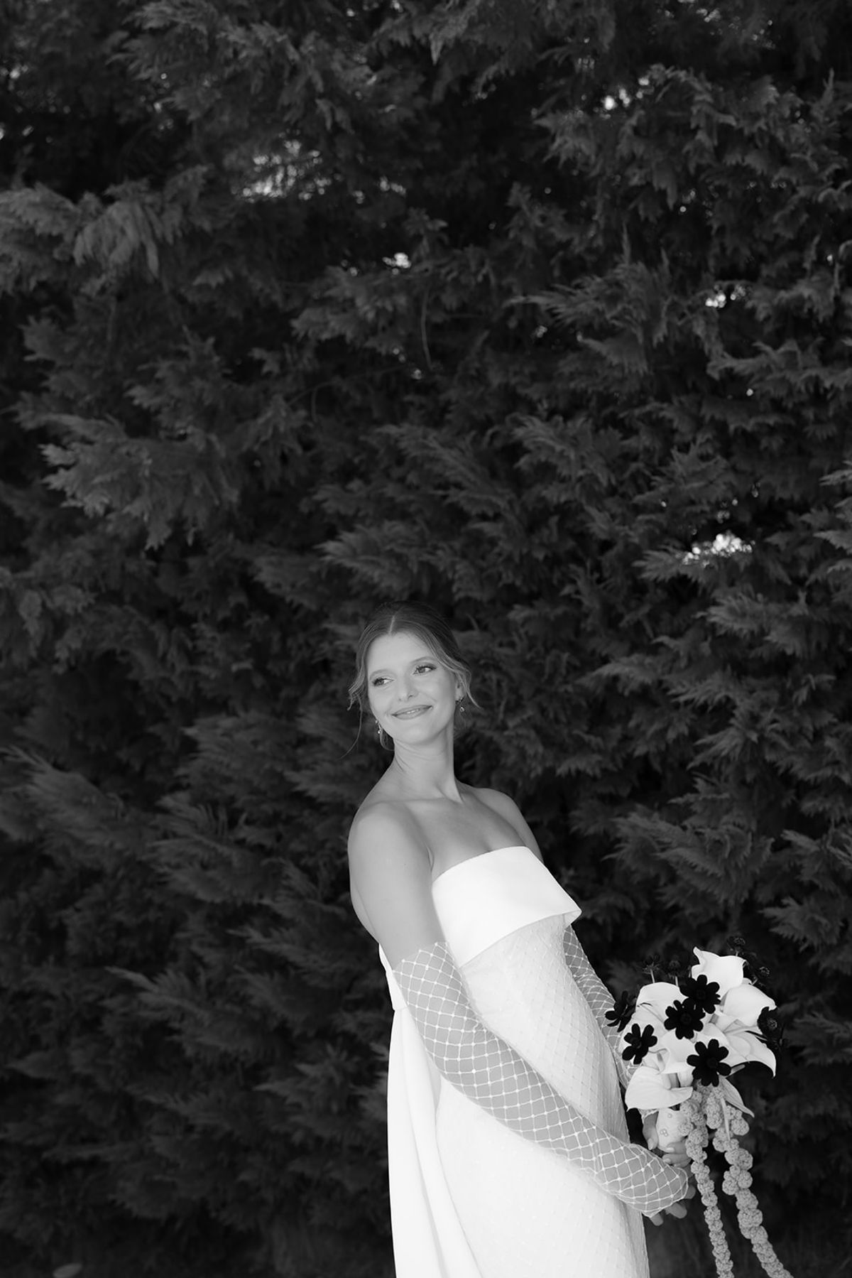 The bride holding her bouquet in front of a dark hedge