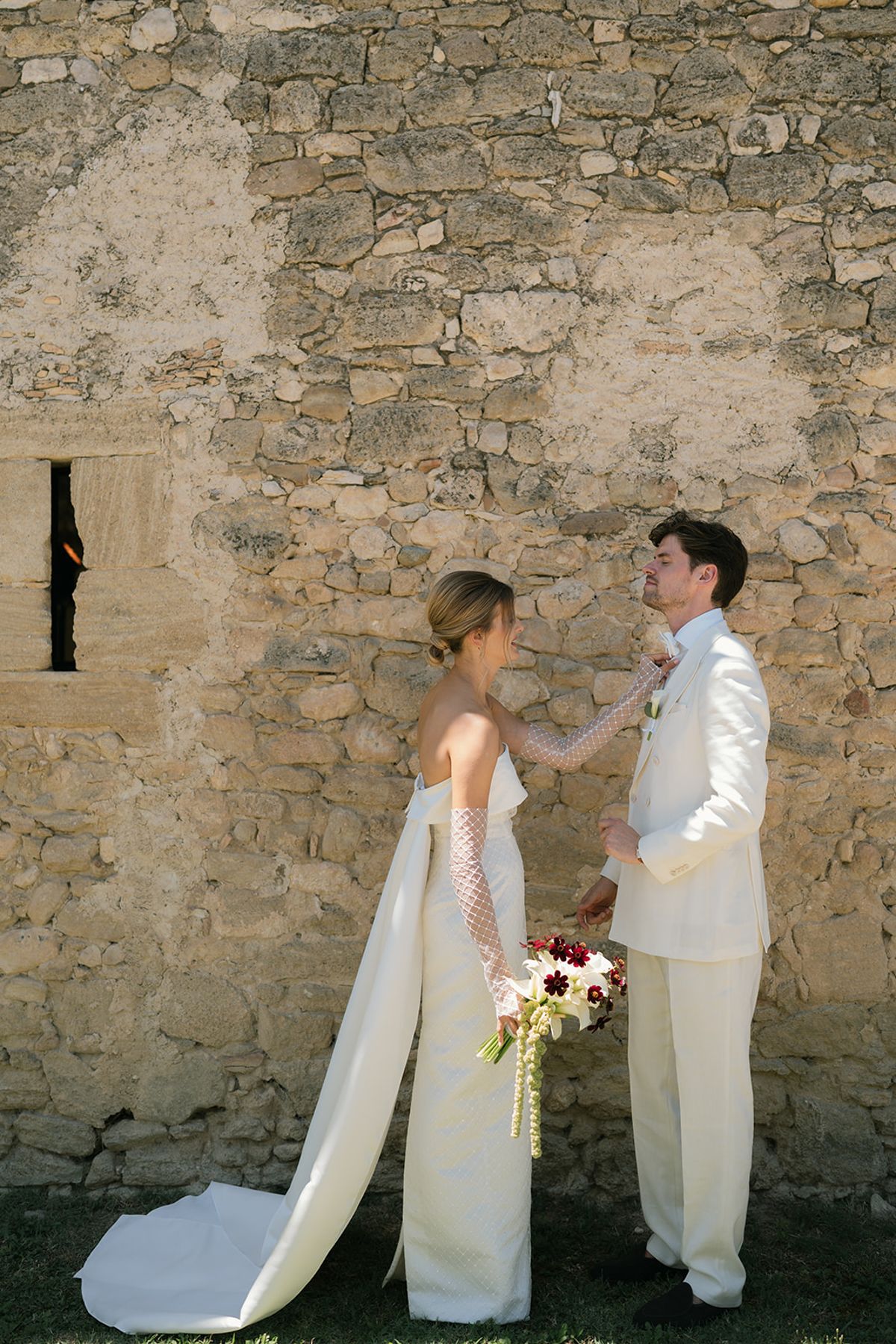 The bride straightens the groom's lapel in front of a stone wall