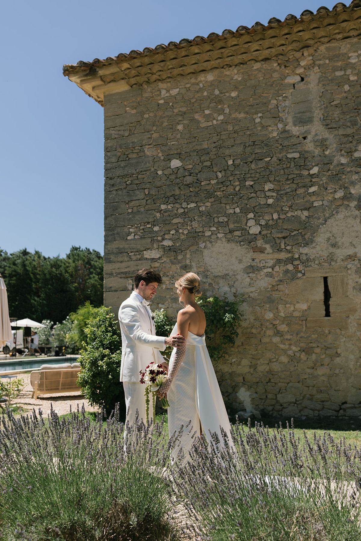 The bride and groom face each other by a stone outbuilding at Le Petit Roulet