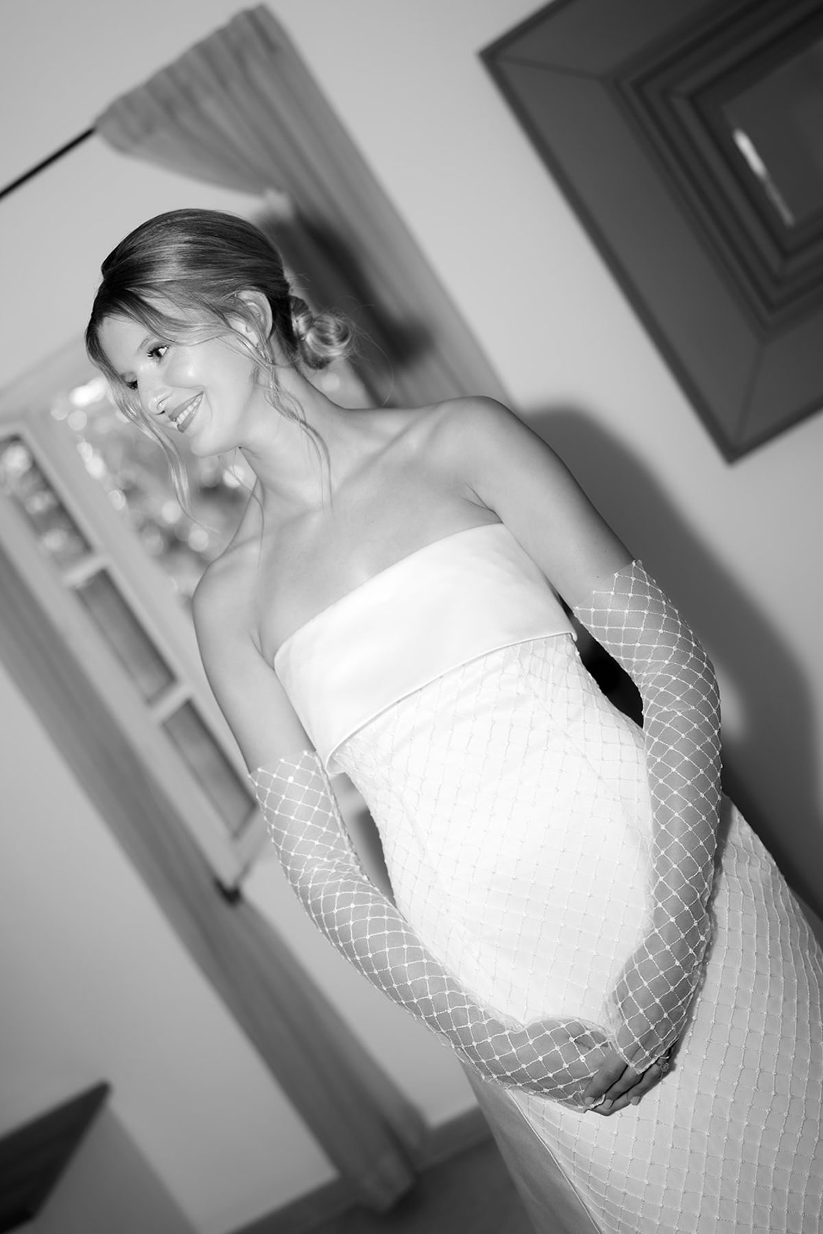 The bride smiling in her bandeau dress and sleeves in a bedroom