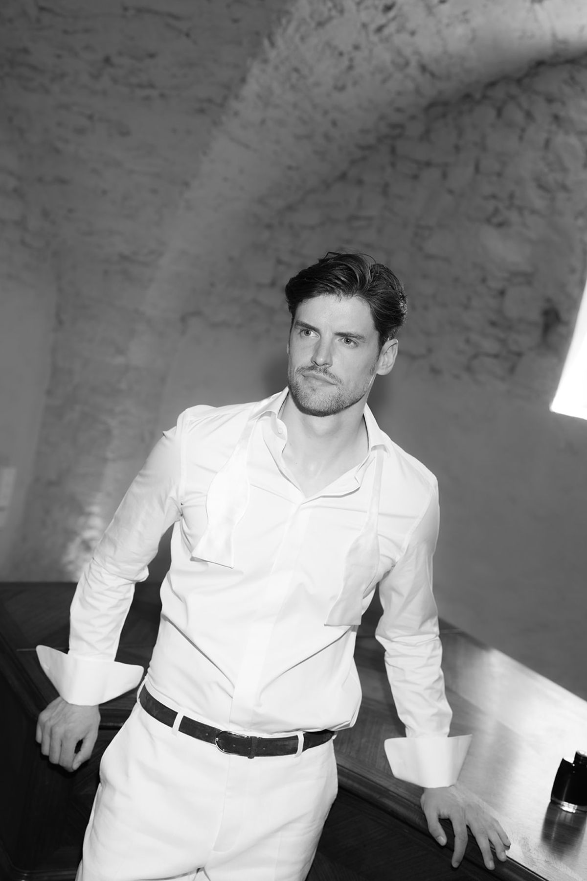 The groom leaning on a table in a vaulted stone room