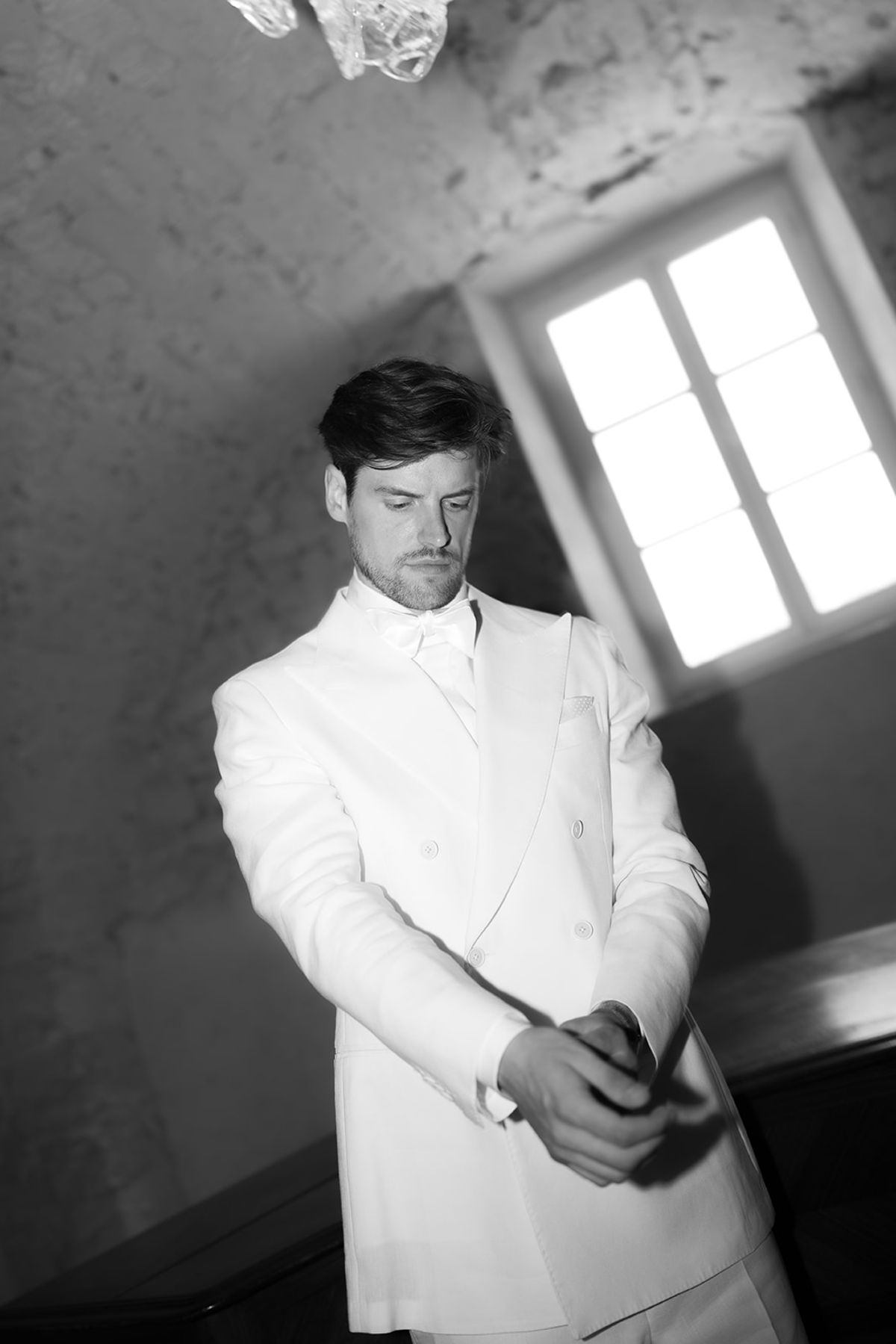 The groom fastening his white double-breasted jacket beneath a vaulted stone ceiling