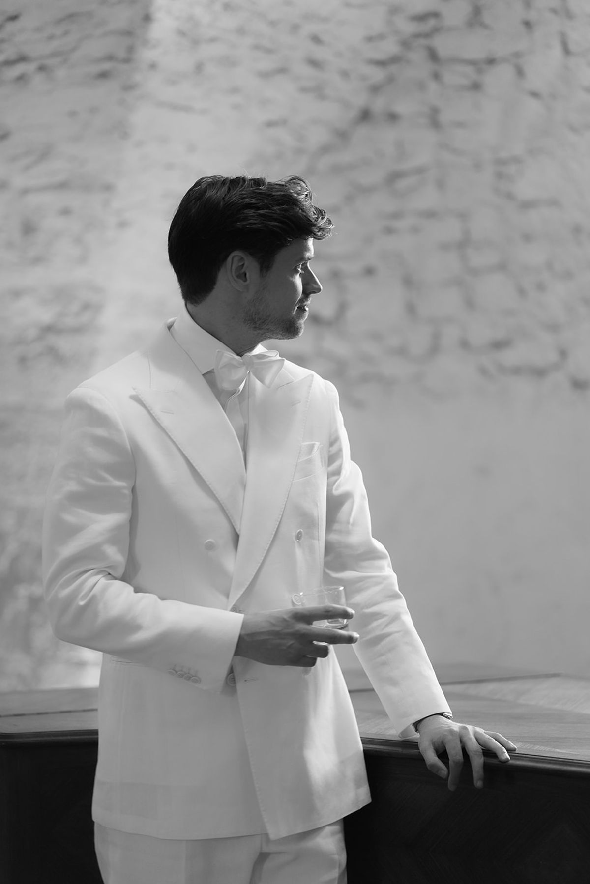 The groom in his white suit and bow tie by a window