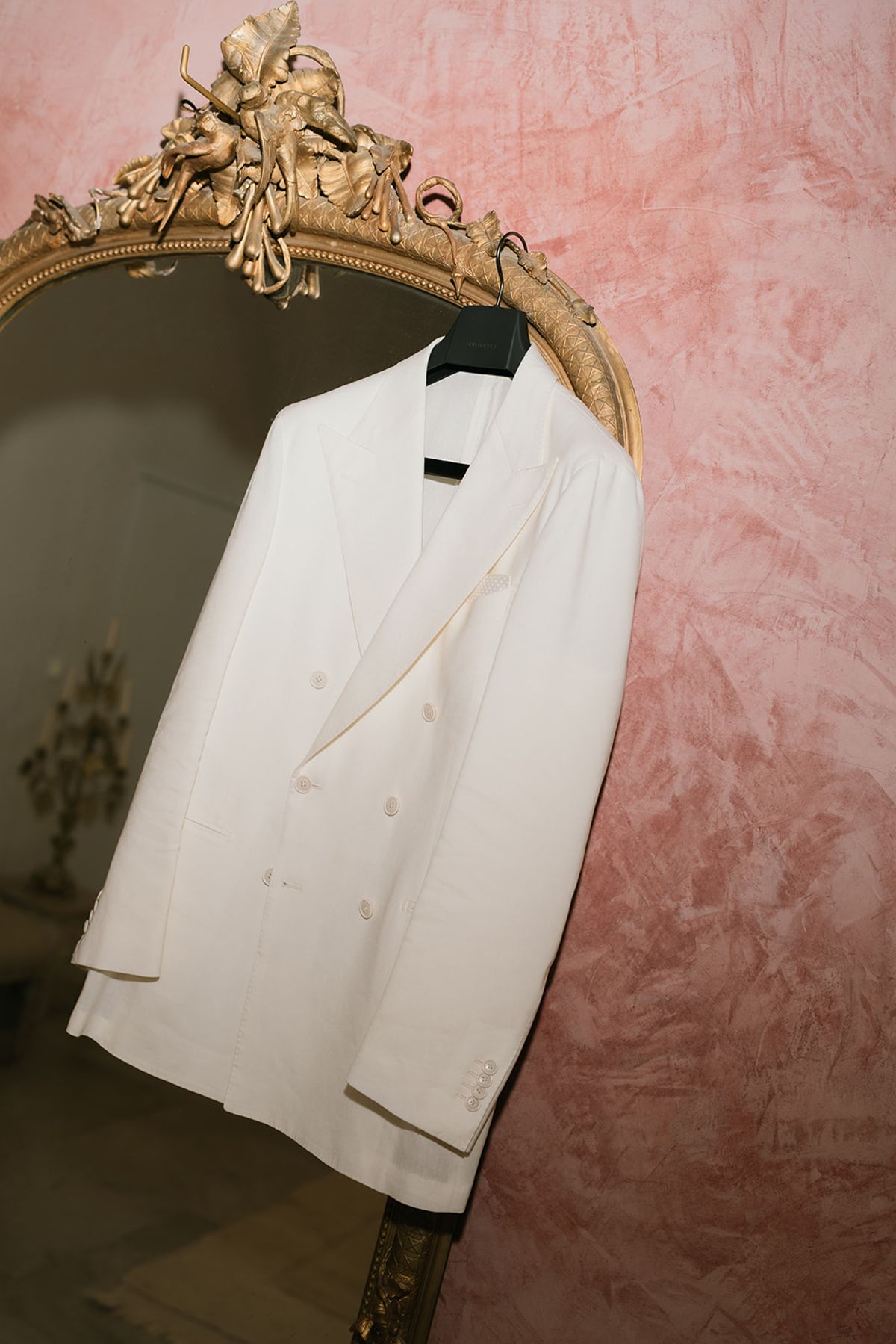 The groom's white double-breasted jacket hanging on a gilt mirror against a pink wall