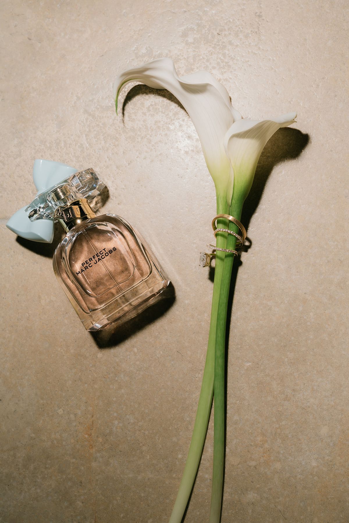 A calla lily with the wedding rings beside a bottle of perfume