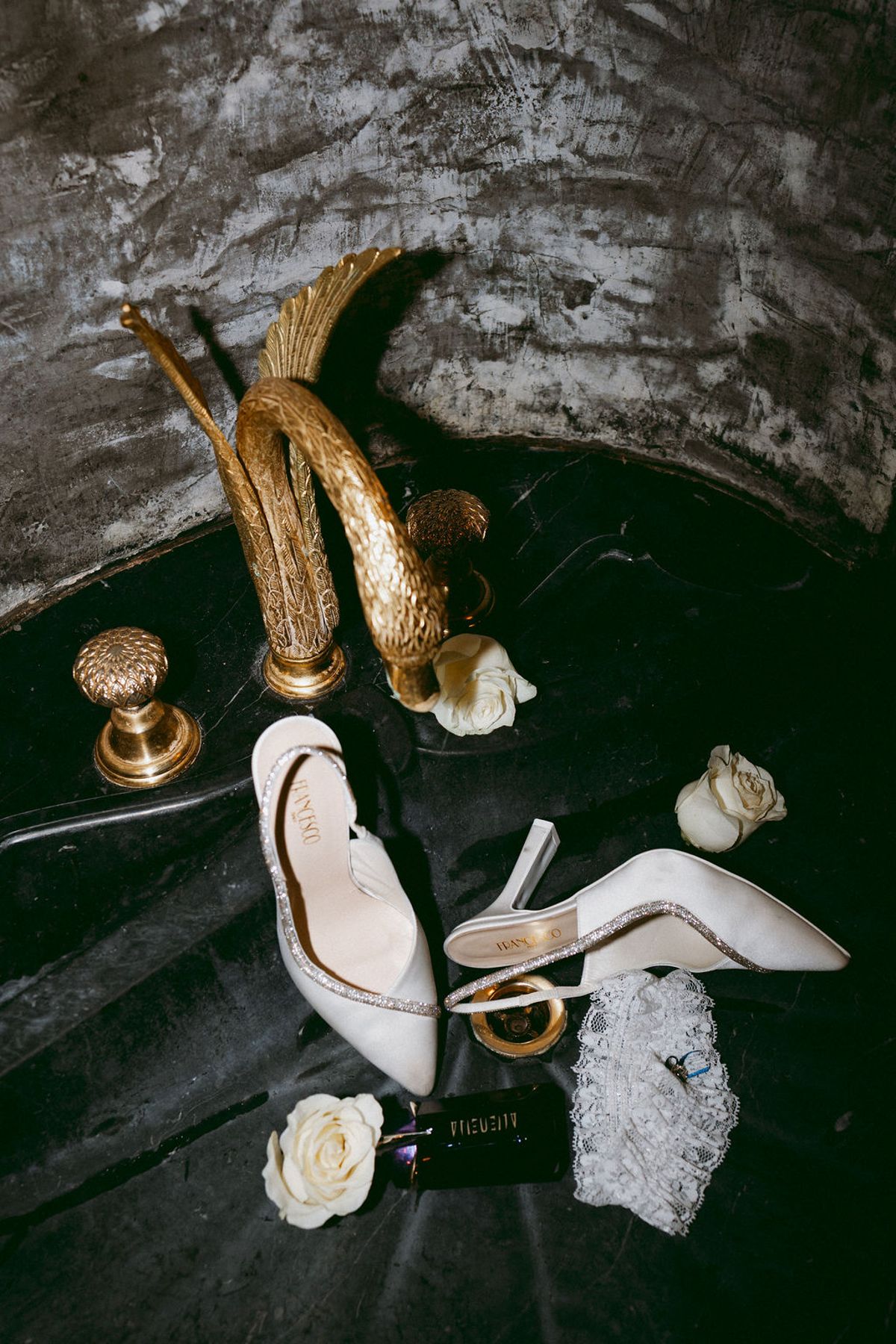 Bridal shoes, perfume and rings arranged with a white rose and gold cutlery