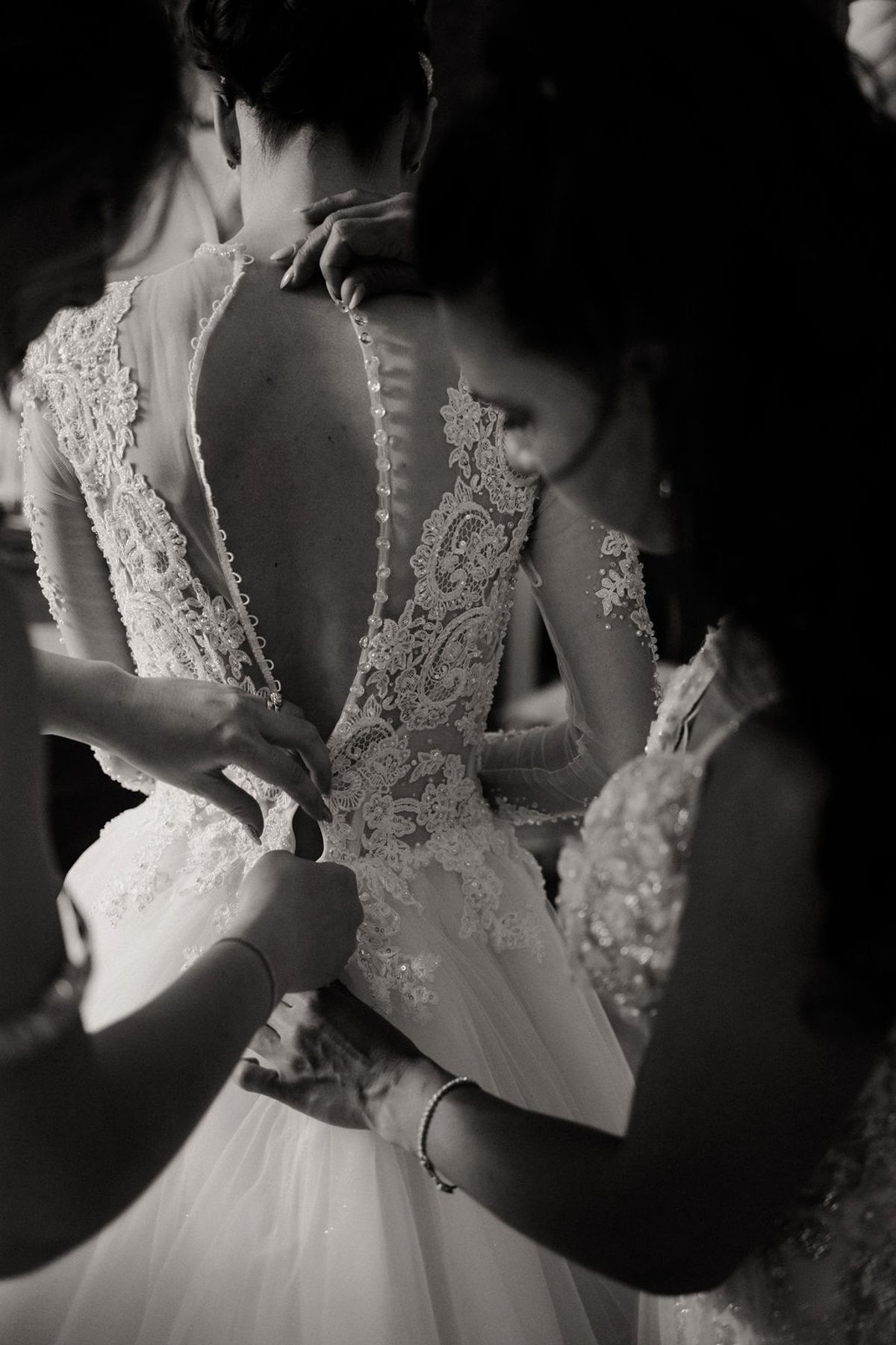 Black and white photograph of the bride being fastened into her lace gown