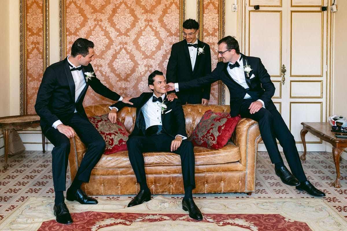 The groom and three groomsmen in black tuxedos seated on a leather sofa