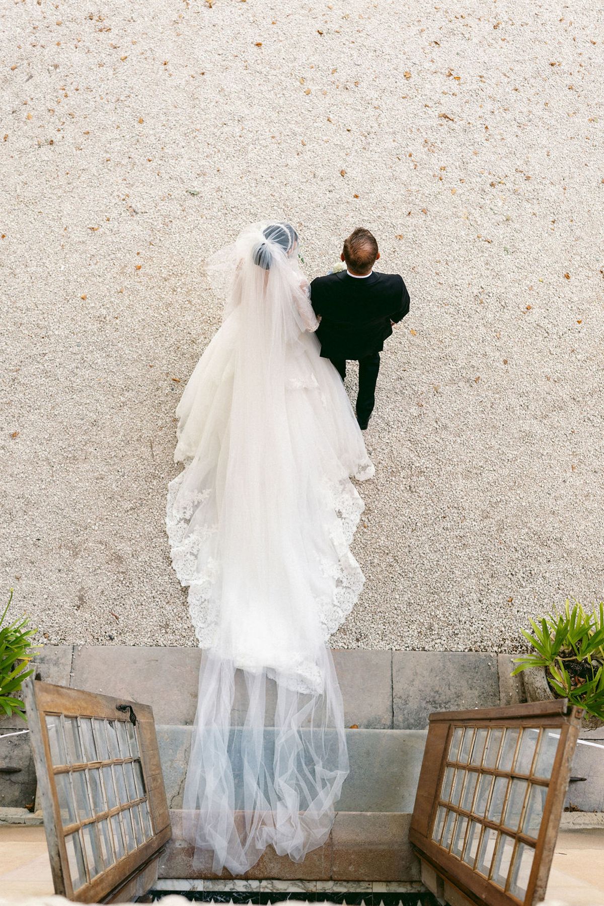 The bride from behind with her veil spread across a stone wall