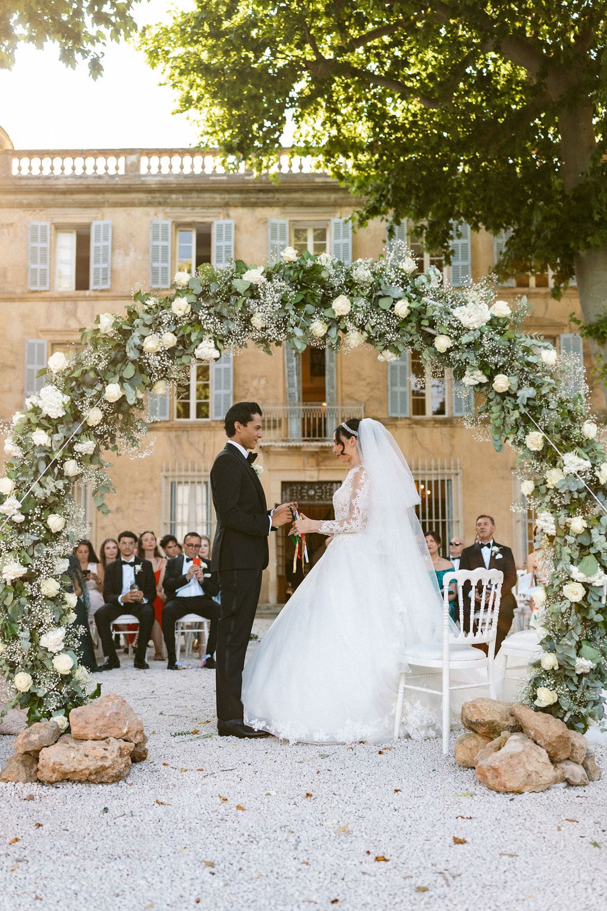 Ilenia and Dalil standing at the floral arch in front of the chateau