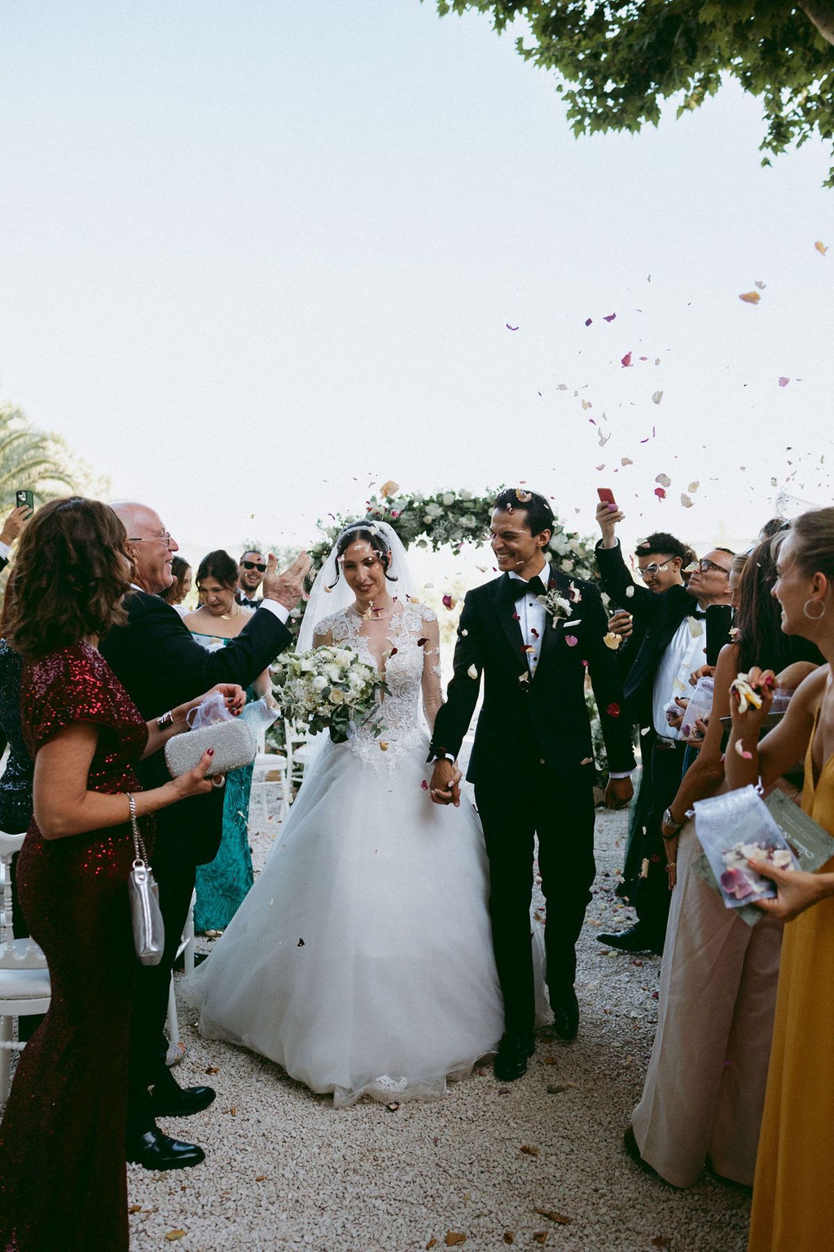 Ilenia and Dalil walking back down the aisle through a shower of petals