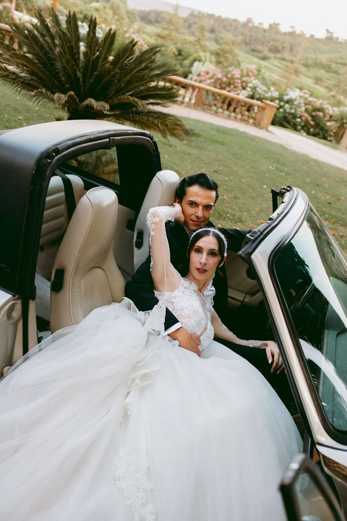 Ilenia and Dalil seated in an open-top car, the bride's gown spilling over the door