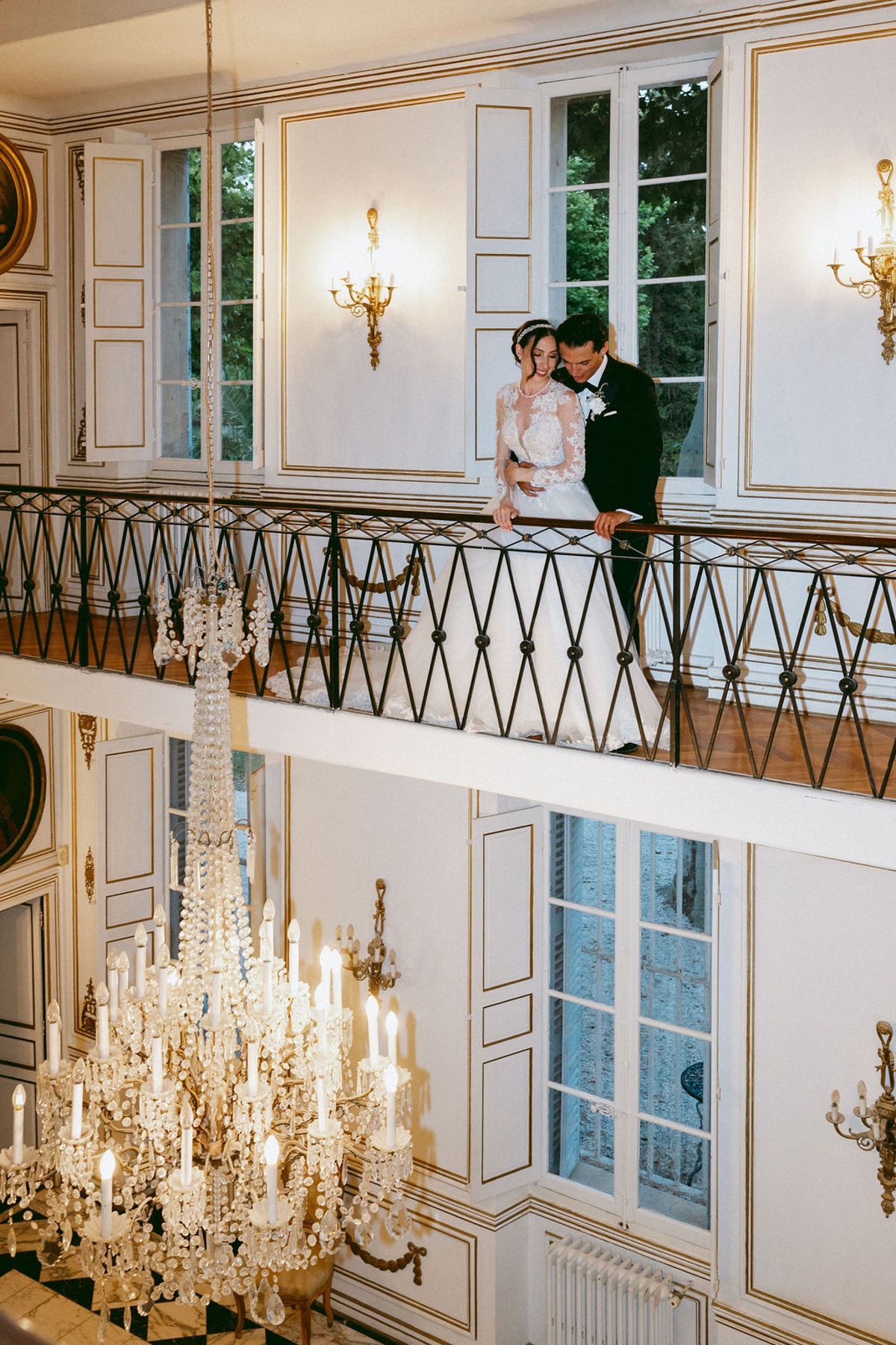 Ilenia and Dalil on an interior balcony beneath a chandelier at Château de Robernier