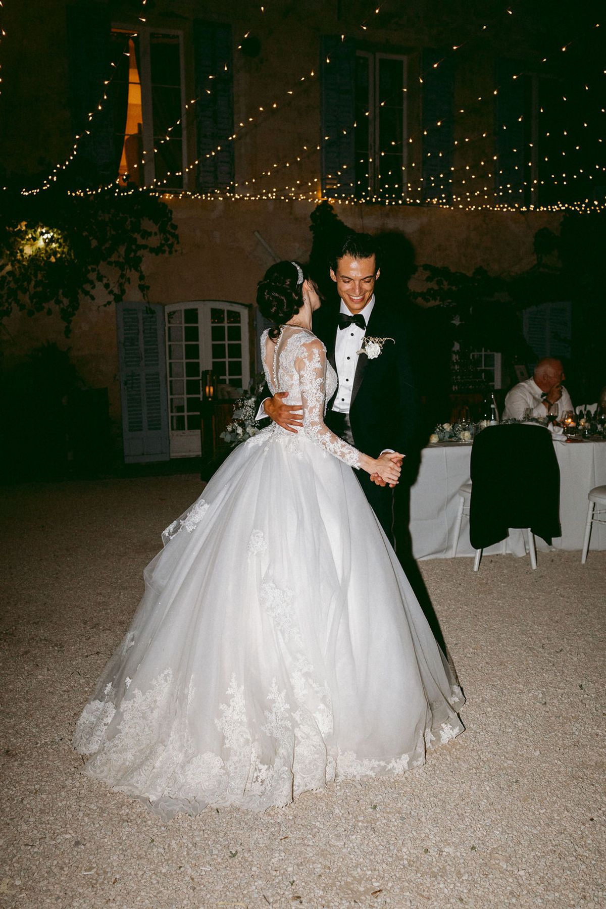 Ilenia and Dalil dancing beneath strings of lights outside the chateau