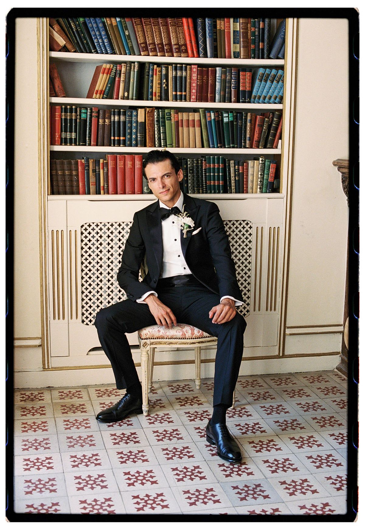 Film photograph of the groom seated before the chateau library bookshelves