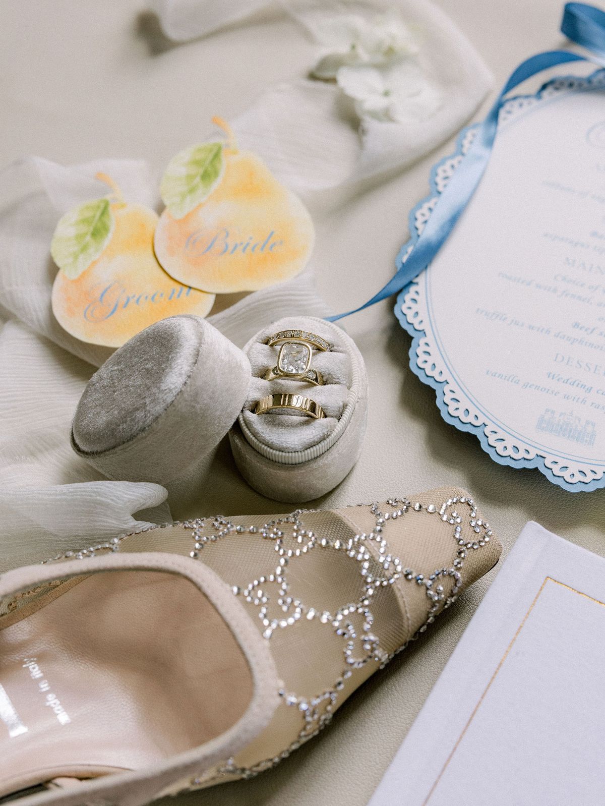 Close-up of the wedding rings in a grey box beside pear-shaped place cards and a blue scalloped menu