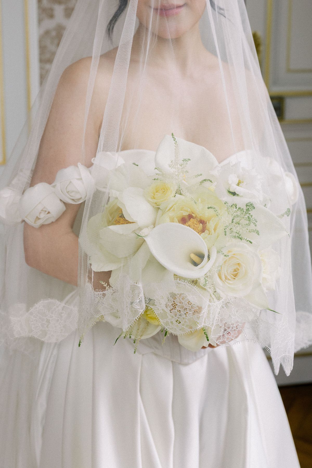 Close-up of the bride's white bouquet of calla lilies and roses seen through her veil